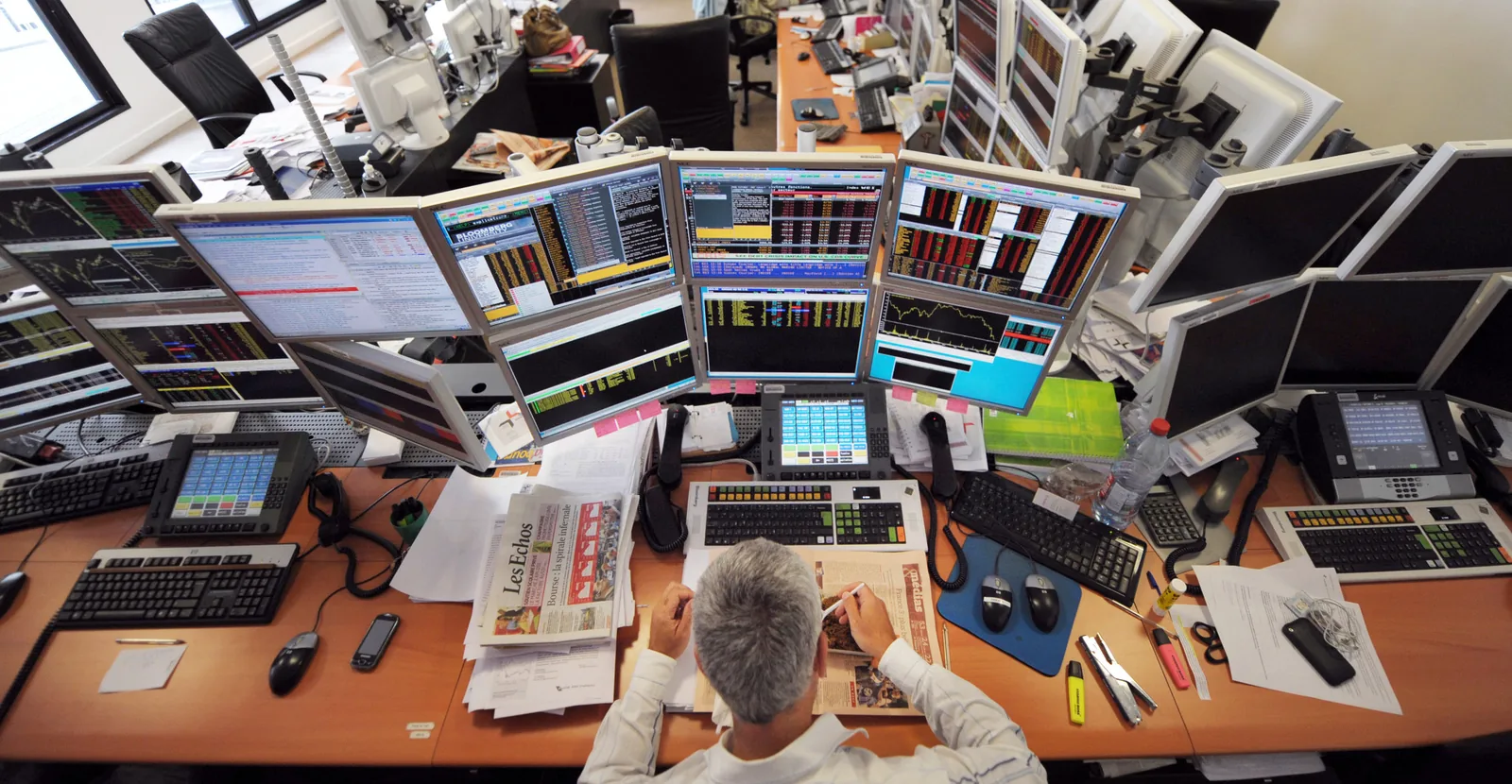 A trader at a desk surrounded by banks of Bloomberg Terminal screens
