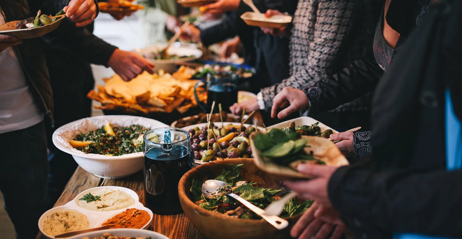 People serving themselves from a long table of shared dishes