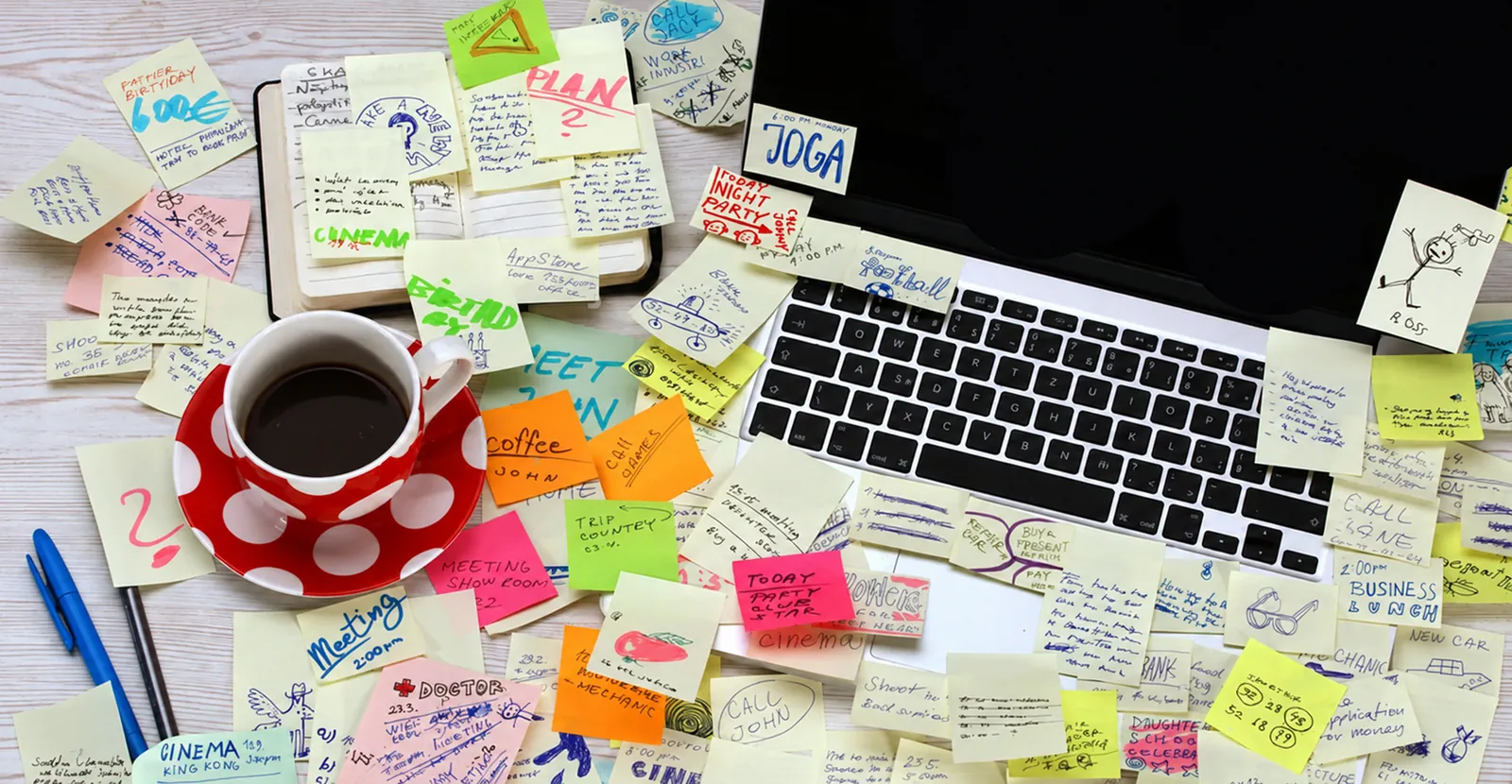 A desk covered in handwritten sticky notes beside a laptop and a coffee cup