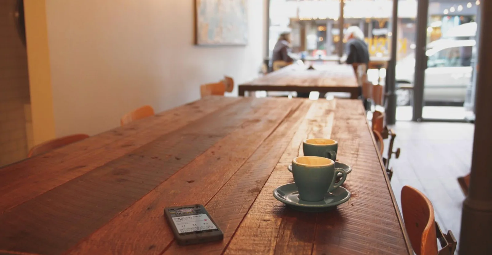 Two espresso cups and a phone on a long wooden café table