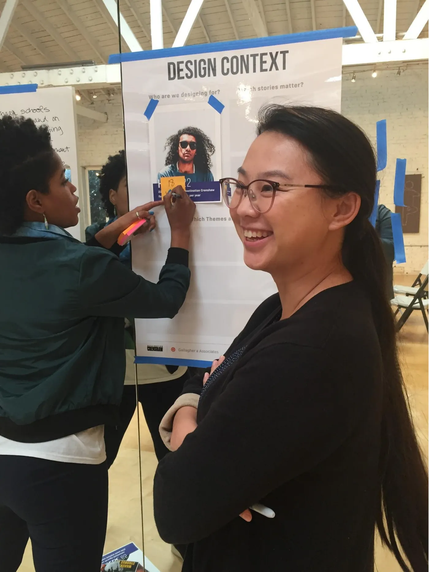 A participant writes on a persona board while another smiles at the camera