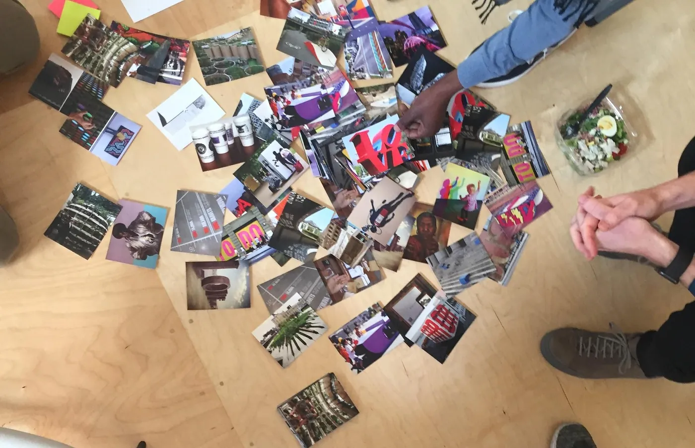 Seen from above, dozens of image cards of Black Los Angeles people, places and moments spread across the studio floor, with participants’ hands and shoes at the edges